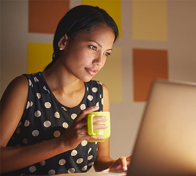 A woman is browsing the internet with a cup of coffee in hand.
